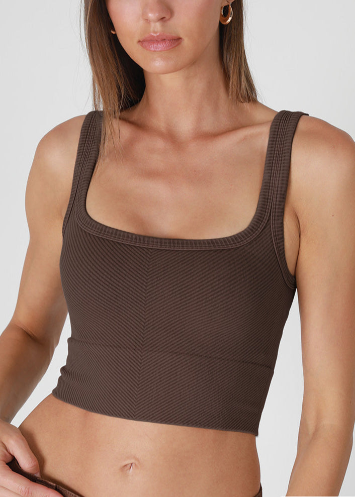woman wearing textured brown tank top on plain background